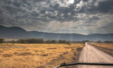 a truck driving down a dirt road under a cloudy sky