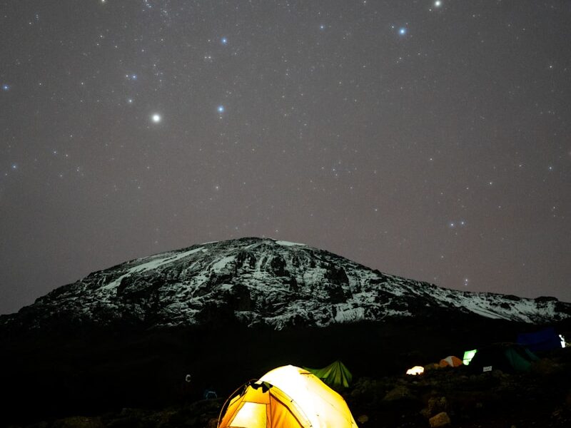 a tent pitched up on a mountain under a night sky filled with stars